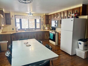 Een keuken met houten kastjes, een witte koelkast, een fornuis en een eettafel met stoelen.