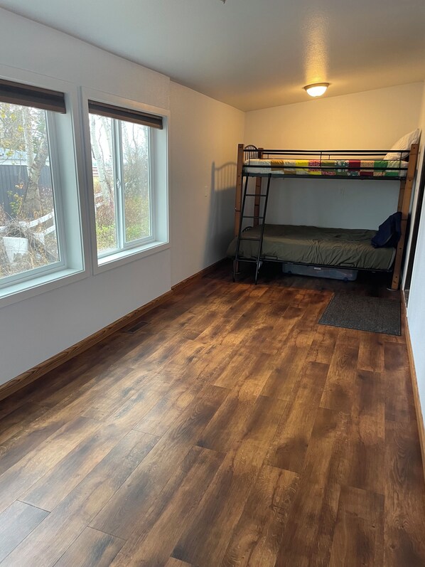 Een kamer met een stapelbed, houten vloeren en twee ramen.