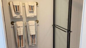 Ein Badezimmer mit Duschabtrennung aus Glas, Holzboden und einem beigefarbenen Teppich.