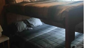 Ein Zimmer mit einem Etagenbett und einem Einzelbett, Holzwänden, einem Fenster und einer Lampe.