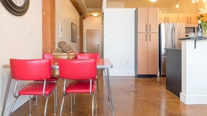 Eine moderne Küche mit Essbereich, ausgestattet mit roten Stühlen und einem Tisch, einem Kühlschrank und einer Wanduhr.