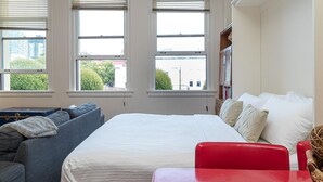 Ein Schlafzimmer mit einem Bett, einem grauen Sofa, einem roten Sessel und einem Fenster mit Jalousien.