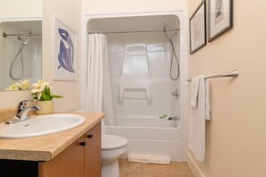 Ein Badezimmer mit Waschbecken, Toilette und Dusche. Ein Handtuchhalter mit einem daran hängenden Handtuch sowie ein gerahmtes Bild an der Wand sind vorhanden.