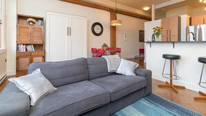 Ein modernes Wohnzimmer mit grauem Sofa, Holzregalen, einer Essecke mit roten Stühlen und einer Küche mit Holzausstattung.