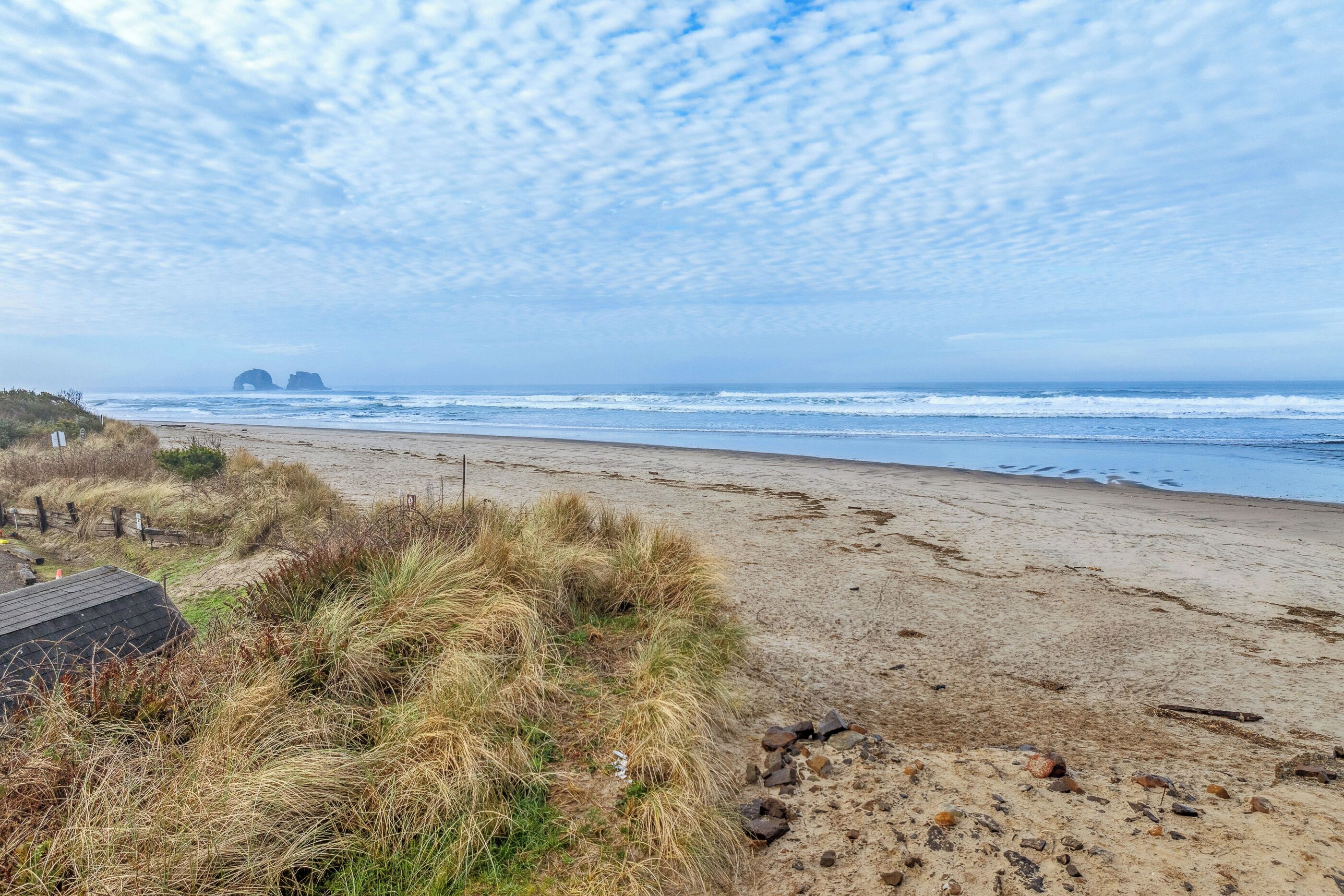 A beach with a sandy shore, grassy dunes, and a distant rocky formation.