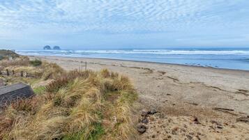 A beach with a sandy shore, grassy dunes, and a distant rocky formation.