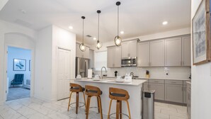 Een moderne keuken met een centraal eiland, barkrukken, roestvrijstalen apparatuur en hanglampen.