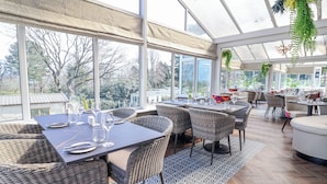 A restaurant with outdoor seating, large windows, and a view of trees. - Woodlands Retreat (Ruthin)