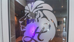 A lion head logo on a glass door, a tiled floor, and a glimpse of a room with a bench and a door. - Woodlands Retreat (Ruthin)