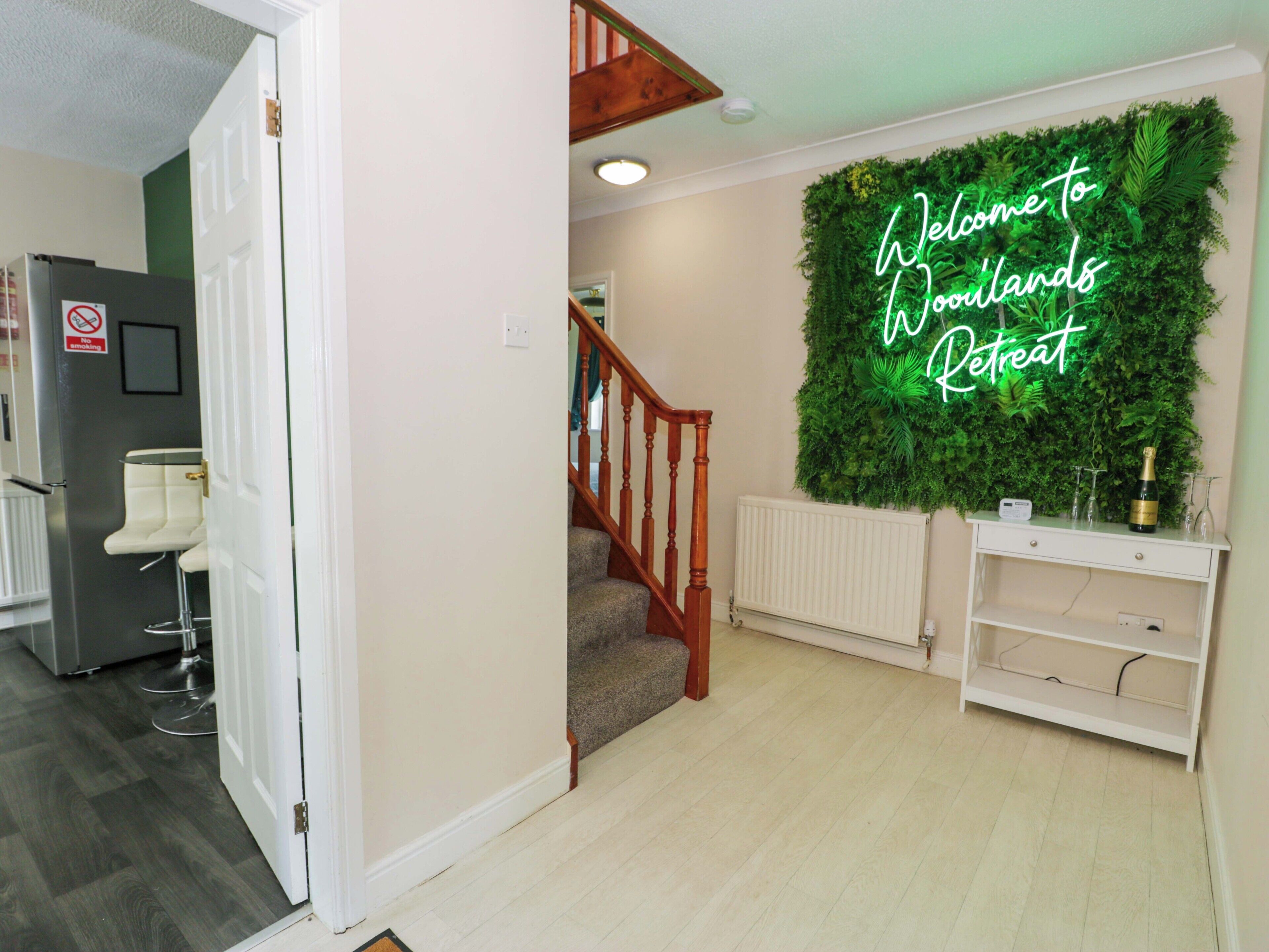 Una habitació amb una escala, un cartell de neó que diu 'Welcome to Holland's Retreat', un radiador i una zona de bar amb una ampolla i gots.