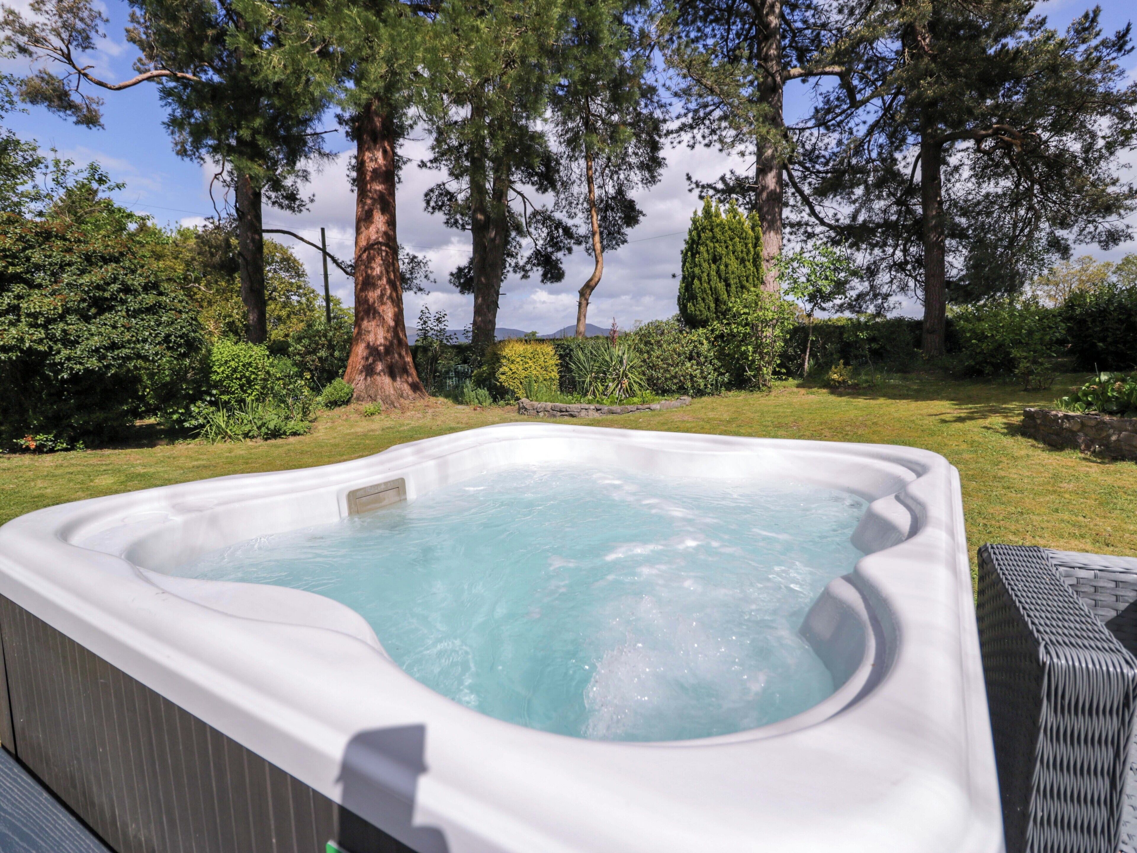 A hot tub in a garden with trees and a stone wall.