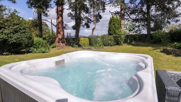 A hot tub in a garden with trees and a stone wall.