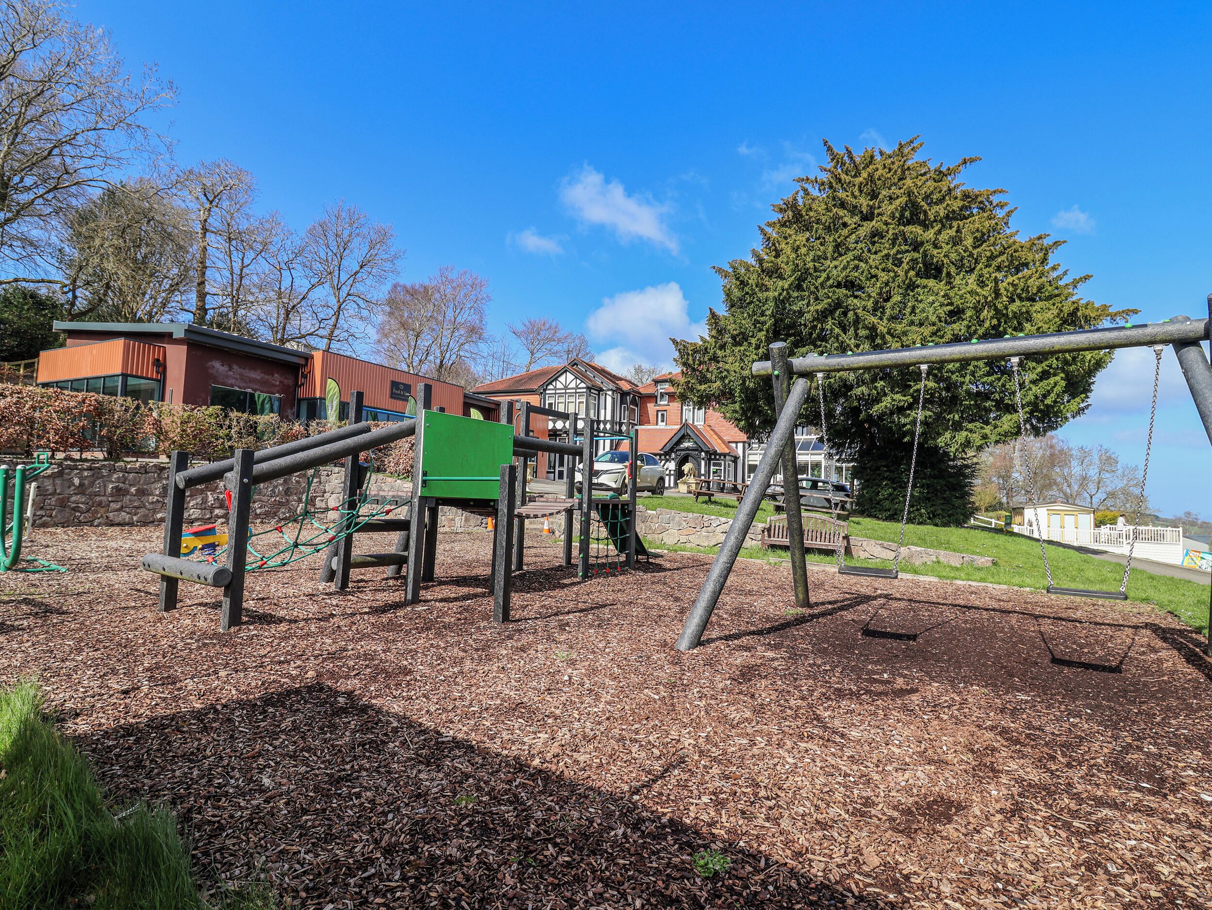 Un parque infantil con columpios y estructuras para escalar, rodeado de árboles y edificios.