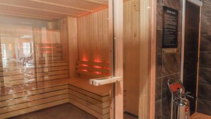 A sauna room with wooden benches, a glass door, a fire extinguisher, and a sign with sauna rules. - Woodlands Retreat (Ruthin)