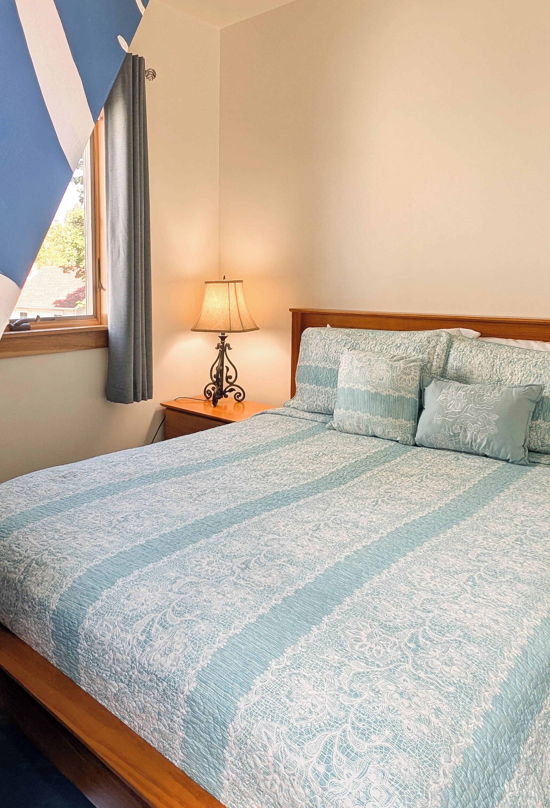 A neatly made bed with a patterned bedspread, a bedside lamp, and a window with curtains.