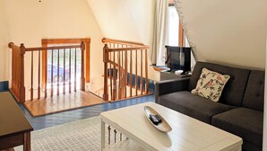 Un salón amplio con techo alto, una escalera de madera, una mesa de centro blanca y un sofá marrón.