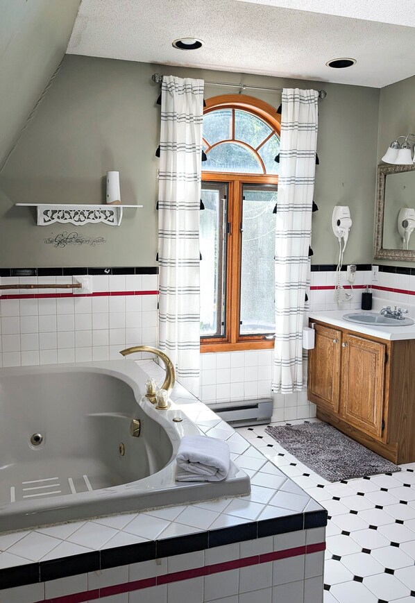 Une salle de bain moderne avec une baignoire sur pieds, un meuble-lavabo en bois, un grand miroir et une fenêtre avec des rideaux.