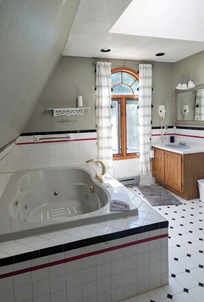 Un baño con una bañera grande, un tocador de madera, un espejo y una ventana con cortinas.