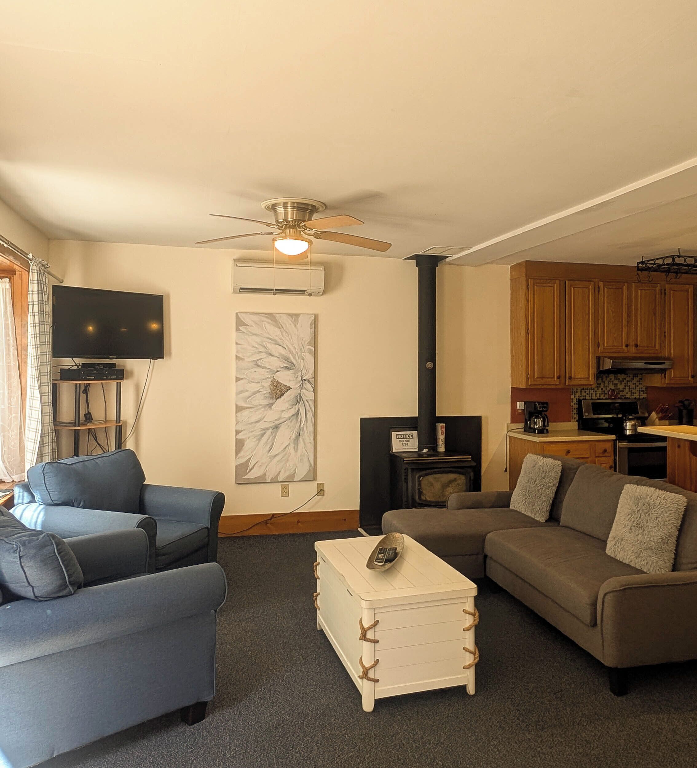 Una sala de estar con dos sofás, una mesa de centro, chimenea, televisor y una cocina con armarios de madera.
