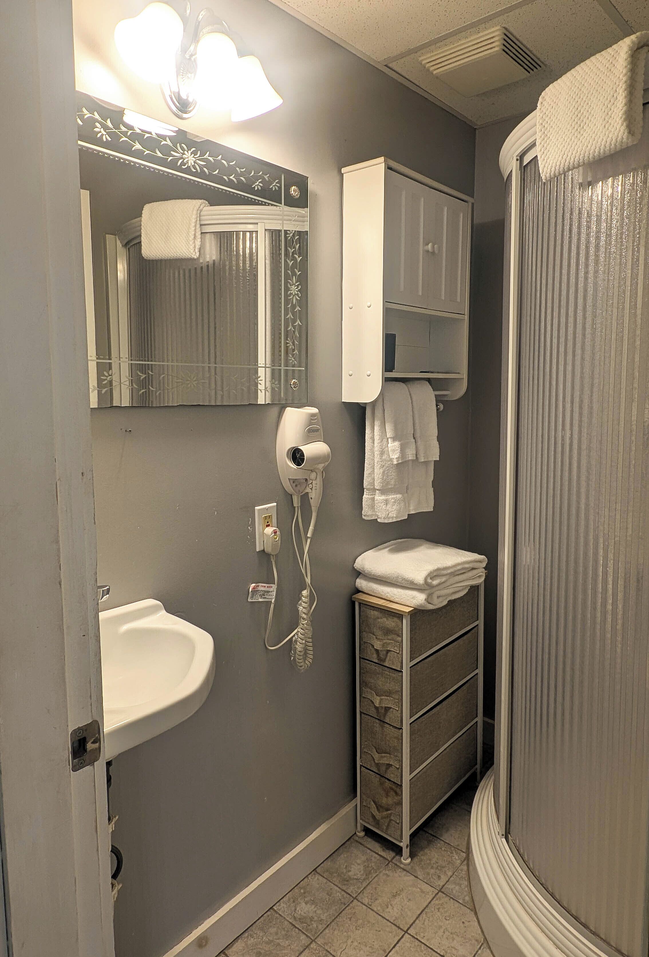 A bathroom with a white sink, a towel rack, a mirror, a hairdryer, and a shower curtain.