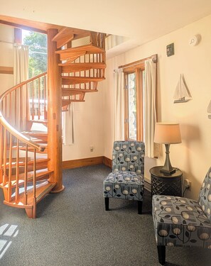A room with a wooden spiral staircase, two patterned armchairs, a small table with a lamp, and a window with curtains. - 3Bedroom2Bath CarriageHouse Pet Friendly (Bar Harbor)