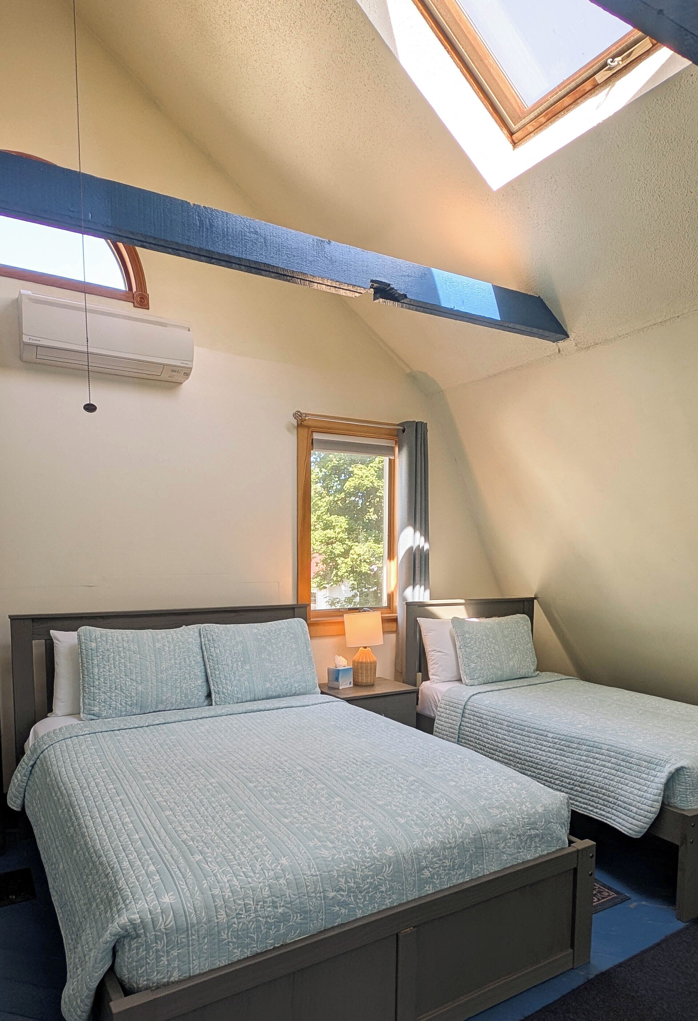A bedroom with two beds, a skylight, and a window.