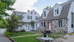 Zona residencial con dos casas, una con fachada de piedra y puerta roja, y otra con exterior blanco y techo gris.
