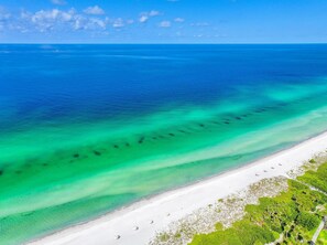 An aerial view of a beach with clear turquoise waters, white sandy shore, and lush greenery. - Full Beach View 2 Bedroom Condo (Longboat Key)