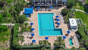 Oversigtsbillede af et resort med en stor swimmingpool, liggestole og palmer.