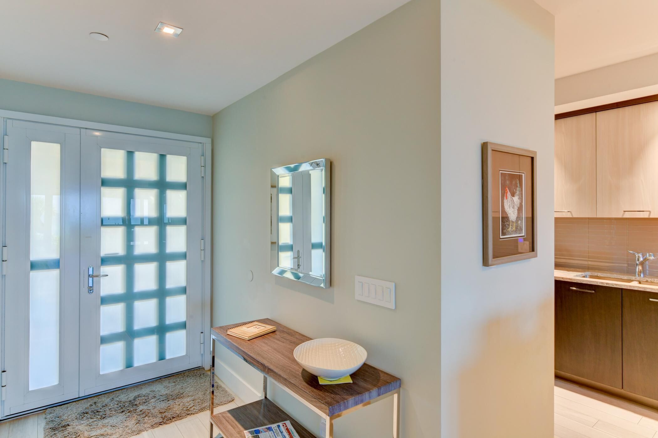 A modern bathroom with a glass door, a wooden vanity, a mirror, and a framed picture on the wall.