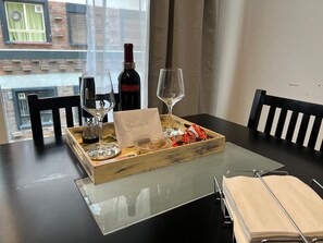 A dining table with a wine bottle, two wine glasses, a card, and a box of chocolates.