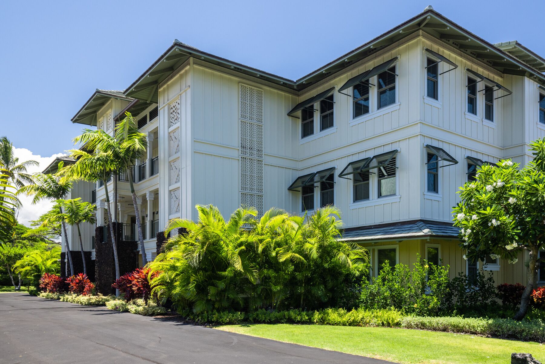 A multi-story hotel with a symmetrical facade, large windows, and a well-maintained garden with tropical plants.