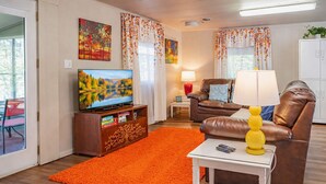 Un salon avec une télévision, un canapé en cuir, un tapis orange et une lampe.