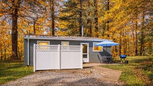 Une petite cabane avec une entrée clôturée, un patio doté d’une table et de chaises, et un barbecue installé à l’extérieur.