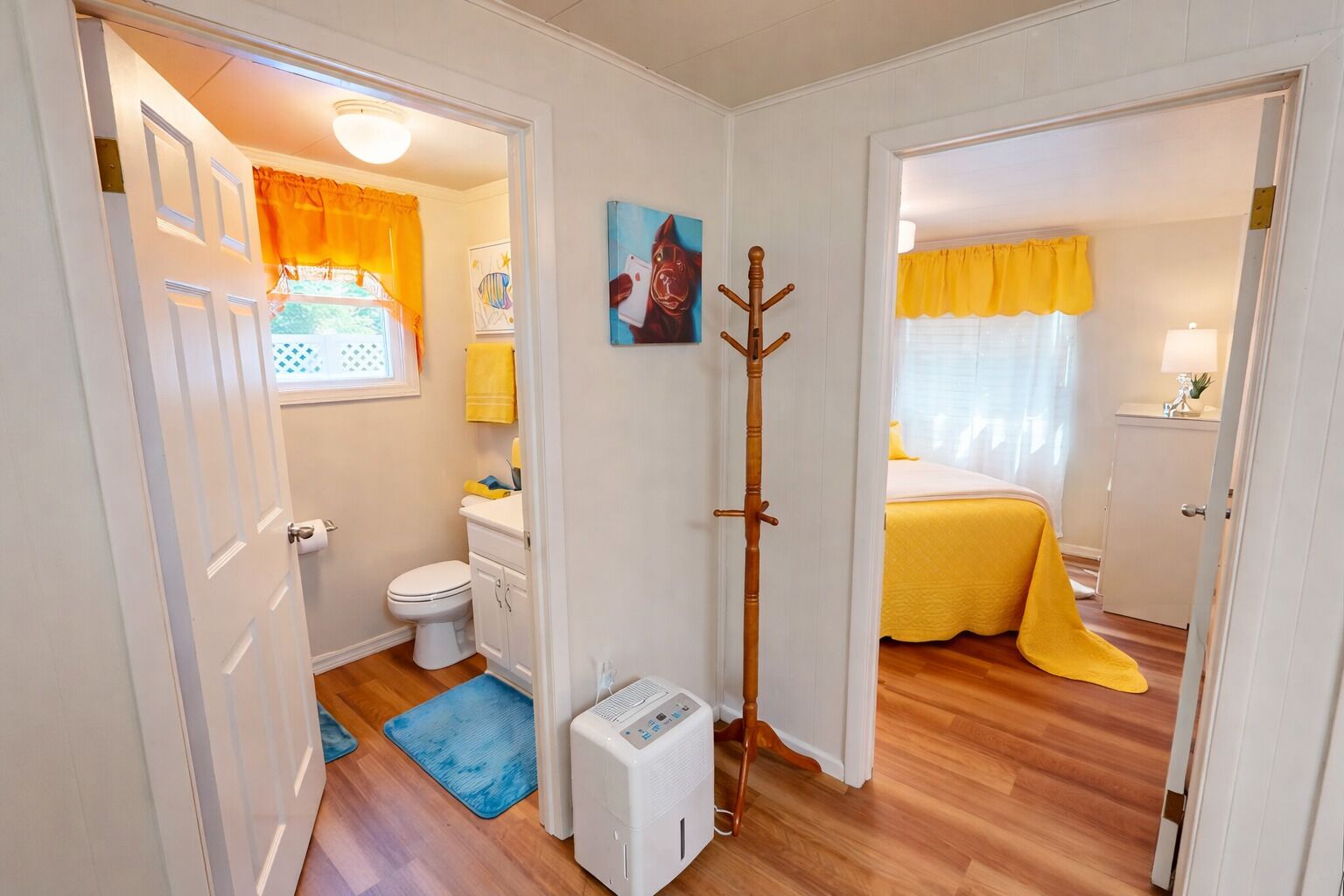 A compact room with a toilet, a bed with a yellow bedspread, a blue mat, and a coat rack.