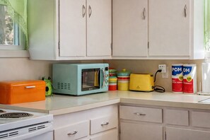 A kitchen with white cabinets, a turquoise microwave, a yellow toaster, and a green frog figurine.