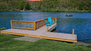 A wooden dock with a bench and a chair, a calm lake, and a forested hill in the background. - Lake Front Oasis: 3 Bed 2 Ba Cottage on Lake Logan (Logan)