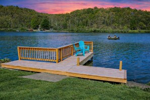 A wooden dock with a bench and a chair, a calm lake, and a forested hill in the background. - Lake Front Oasis: 3 Bed 2 Ba Cottage on Lake Logan (Logan)