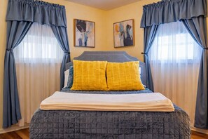 Ein Schlafzimmer mit einem Bett, zwei Kissen, einem Kopfteil und Vorhängen.