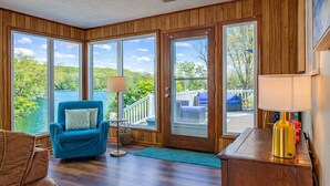 A room with a view of a lake, a blue chair, a lamp, and a wooden desk. - Lake Front Oasis: 3 Bed 2 Ba Cottage on Lake Logan (Logan)