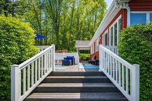 Eine Holzterrasse führt zu einem überdachten Außenbereich mit Esstisch und Stühlen.