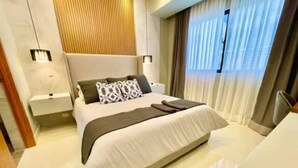 A modern bedroom with a large bed, bedside tables, a headboard, and a window with curtains.