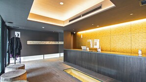 A reception area with a modern design, featuring a reception desk, a seating area with stools, and a large window providing natural light. - HOTEL NINJA BLACK (Kyoto)