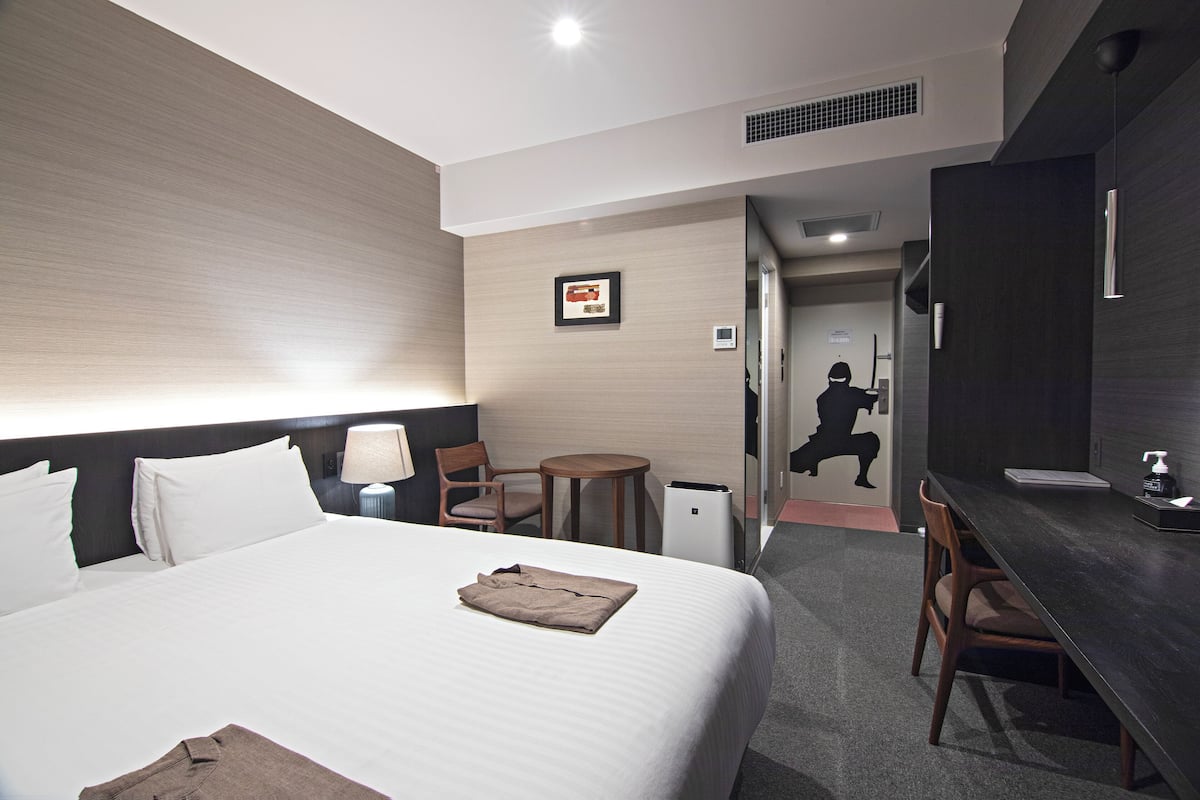 A hotel room with a large bed, a desk, a chair, a small table, and a mirror.