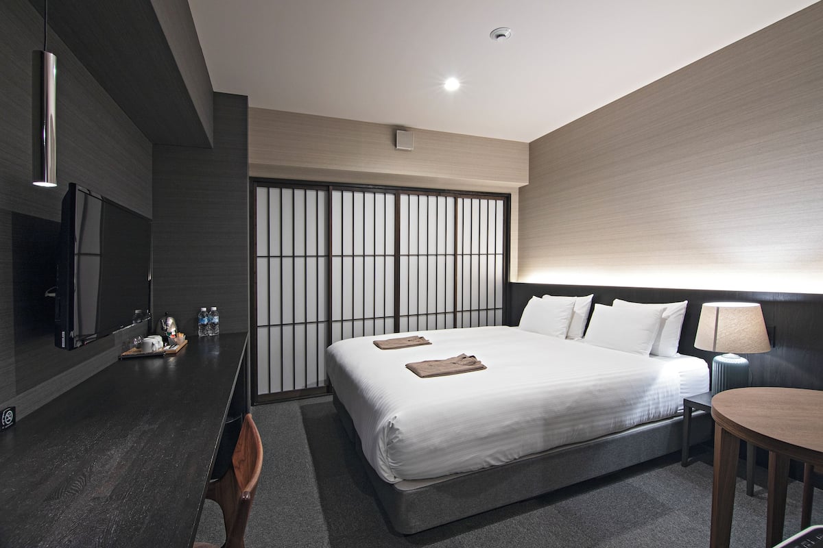 A modern hotel room with a large bed, bedside table, and a TV.