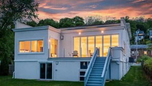 Una casa moderna de dos pisos con ventanas amplias, un porche cubierto y una escalera que conduce al nivel superior.