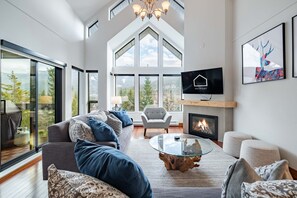A modern living room with a large sofa, a glass coffee table, a fireplace, and a TV mounted on the wall. - Mountain views | Free parking | BBQ | AC (Whistler)