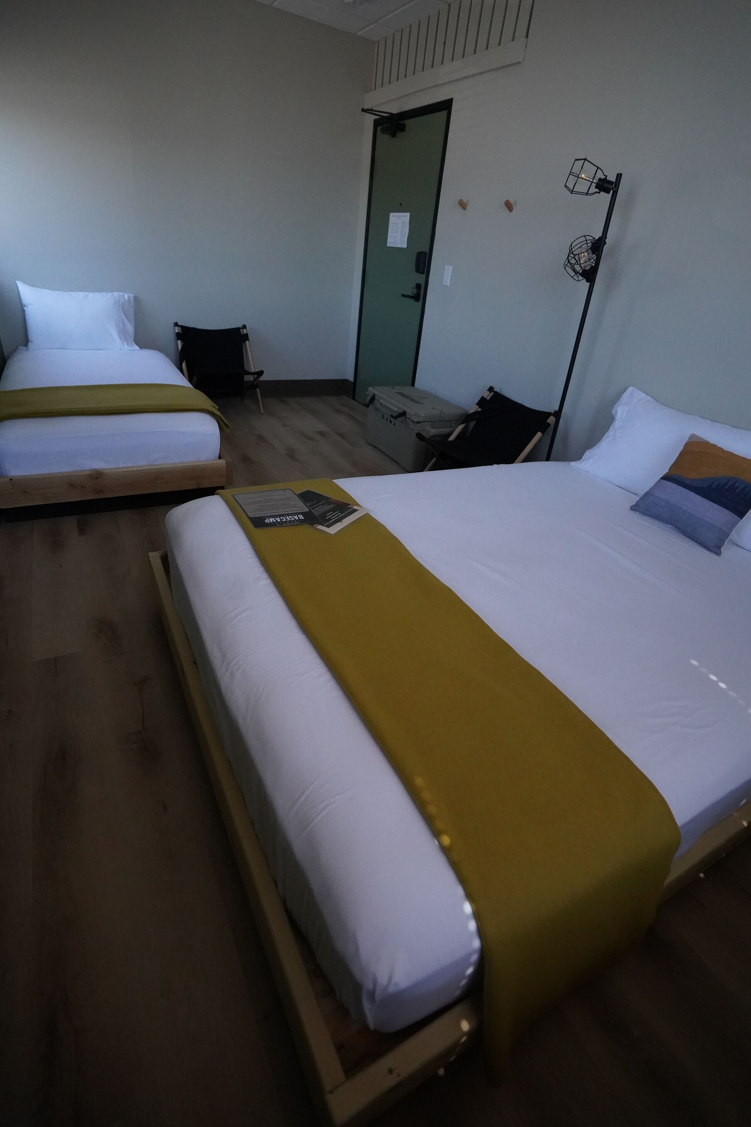 A hotel room with two single beds, a desk, a chair, and a door.