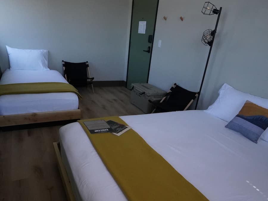 A hotel room with two single beds, a desk, a chair, and a door.