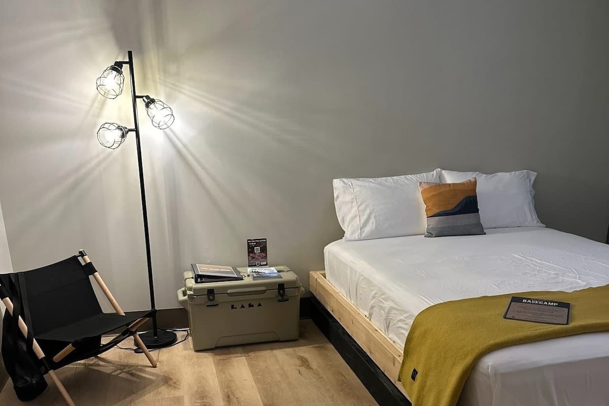 A bedroom with a bed, a chair, a suitcase, and a floor lamp.